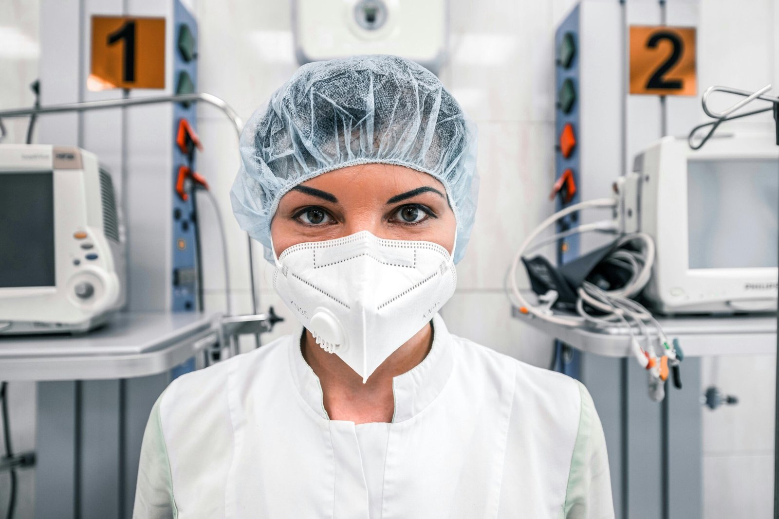 Home Female healthcare worker in a hospital wearing a mask and surgical cap, standing confidently.