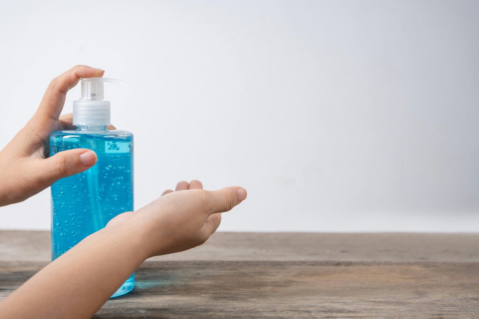 Home Close-up of child's hands using a blue sanitizer dispenser on a wooden surface.