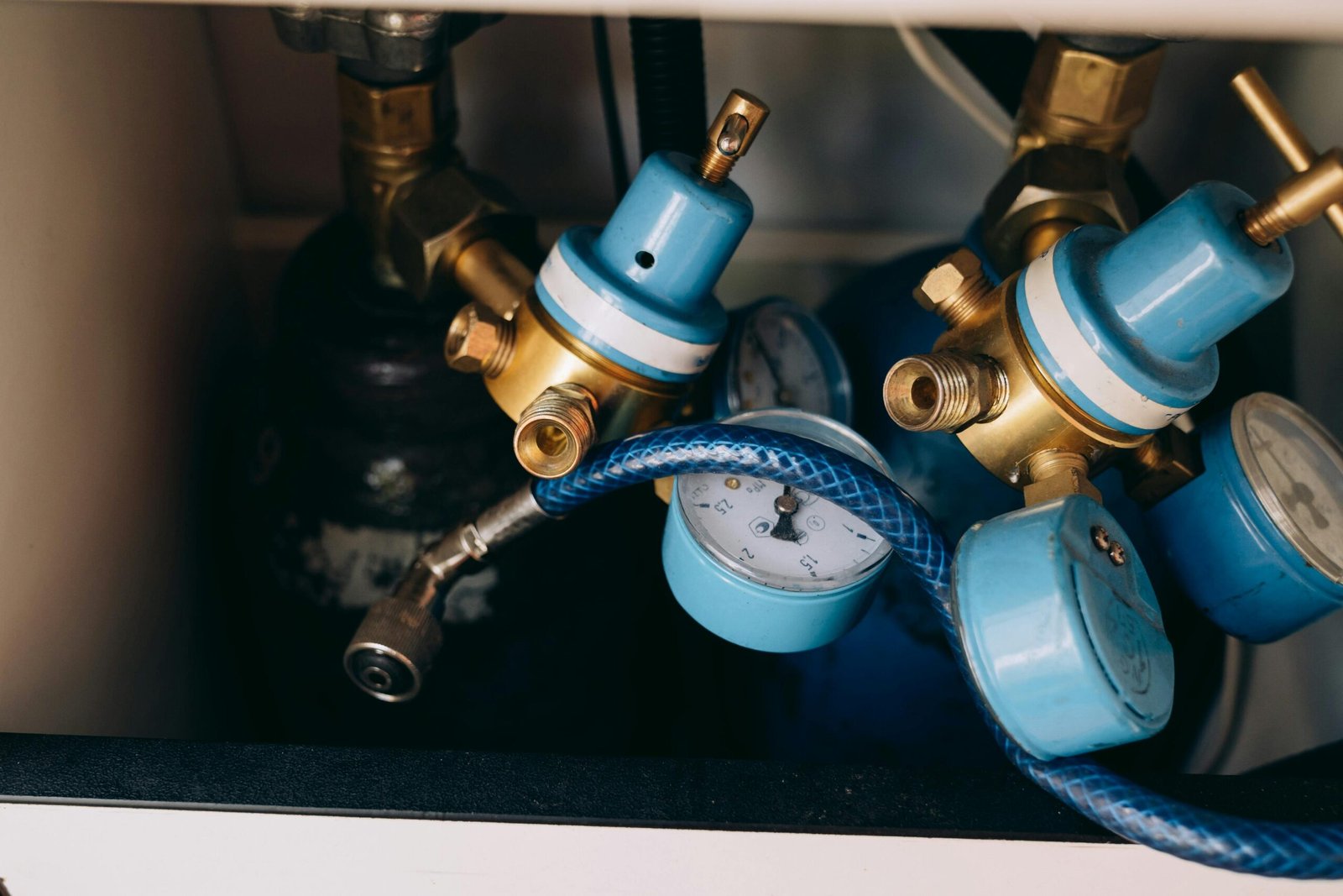 Home Detailed view of blue and brass gas pressure regulators with gauges and tubing in an industrial setting.